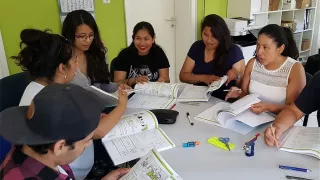 Gruppe aus sechs jungen Freiwilligen sitzt mit Textbüchern in in der Hand an einem Tisch und unterhält sich.