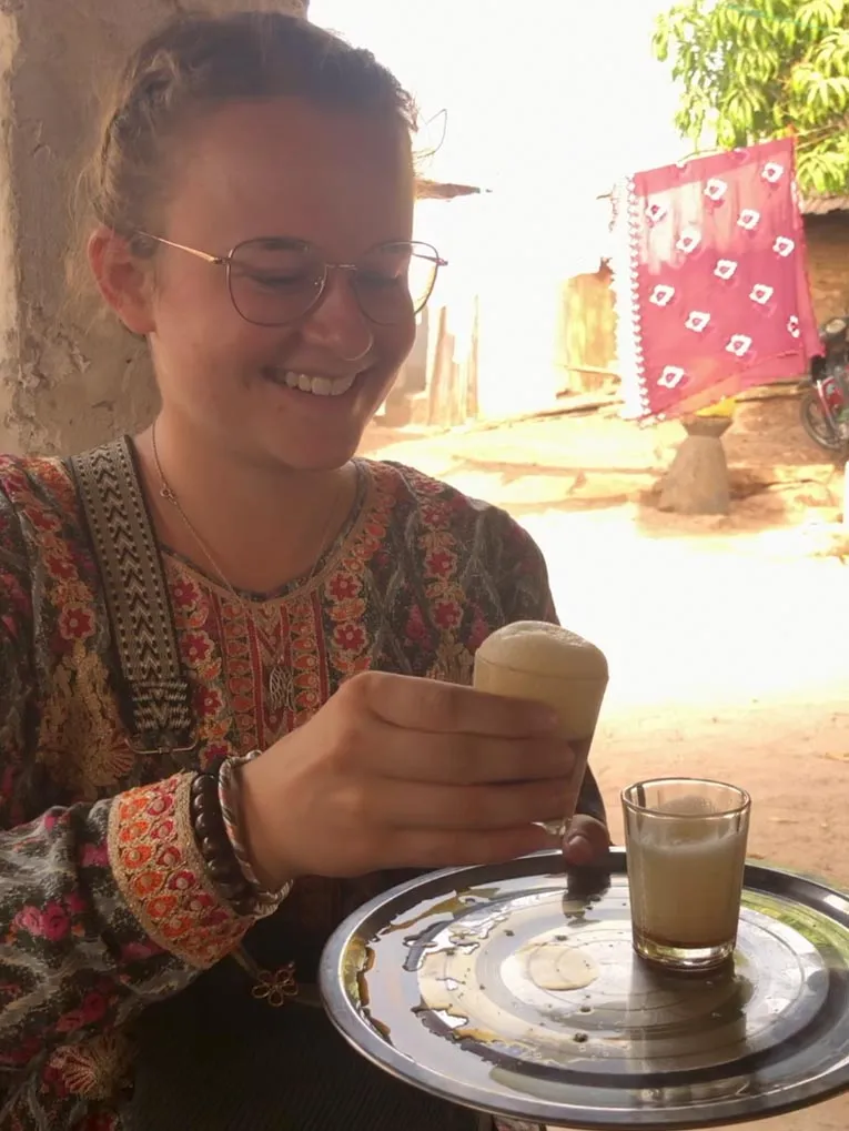 Eine Frau lacht in die Kamera während sie ein milchschaumartiges Getränk trinkt.